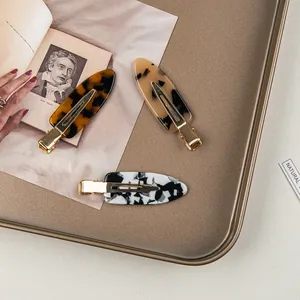 Close-up of three acetate hair clips in tortoiseshell and marble patterns with gold metal