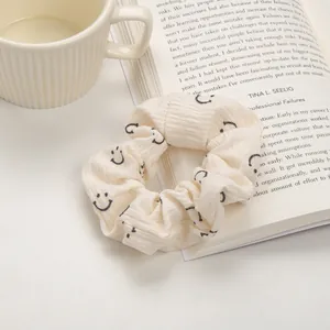 Détail du chouchou plissé crème avec motifs smiley et texture de tissu côtelé