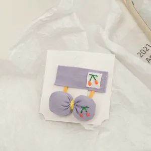 Detail of purple fabric hair set featuring cherry embroidery on bow tie and rectangular clip