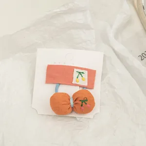 Detailed shot of fabric hair clip set featuring orange bows and cherry embroidery accents
