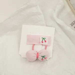 Detail of pink fabric hair clips and bow with cherry embroidery on a display card