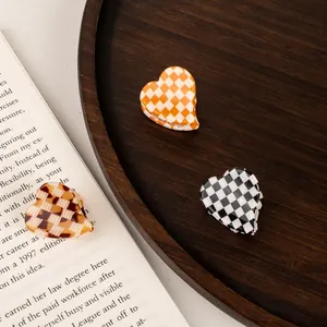 Three mini acetate heart hair claws in checkered patterns on a vintage wooden tray