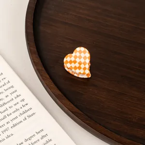 Detail of a mini heart-shaped acetate hair claw featuring orange and white checkerboard pattern