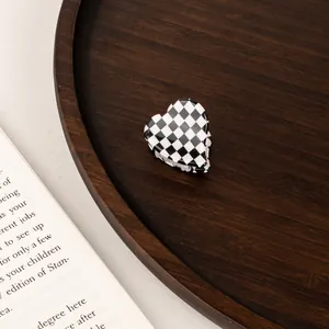 Detailed view of a mini heart-shaped checkerboard hair claw clip on a rustic wooden tray