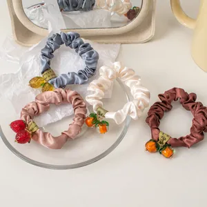 Set of four satin scrunchies in pastel colors featuring glossy fruit charms on a tray