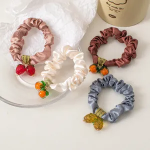 Detailed view of satin scrunchies with cute fruit charms in multiple soft colors