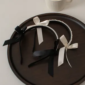Detail of double-row pearl headbands with black and cream silk bows on a wooden tray