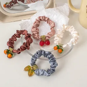 Detail of four satin scrunchies with fruit charms on a glass plate and cream mug