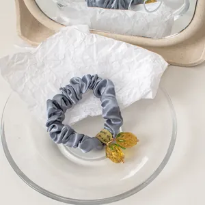 Close-up of a grey satin scrunchie featuring cute translucent yellow pineapple charms