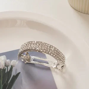 Close-up of curved silver hair clip with sparkling rhinestones on a white plate