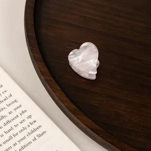 Close-up of a pearlescent white acetate heart hair claw clip on a dark wooden tray