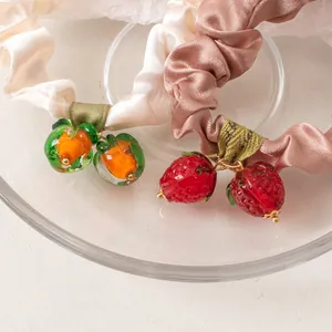 Close-up of cream and red satin scrunchies with glass-like persimmon and strawberry charms