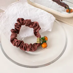 Detail shot of brown satin scrunchie with a cute orange pendant in a glass tray