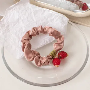 Detail of pink silk hair scrunchie with red strawberry pendant and leaf charm decoration