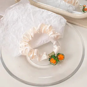 Detail of cream satin scrunchie with orange persimmon fruit pendant and green leaves