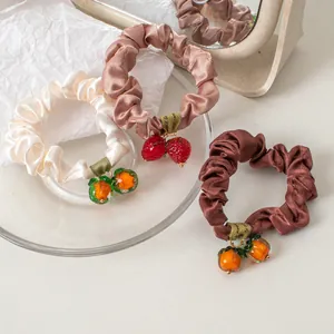 Detailed close-up of three satin scrunchies with glass fruit charms in sweet girl style