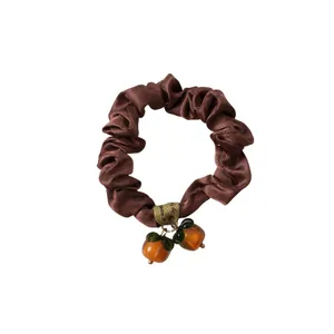 Brown satin scrunchie with orange persimmon fruit pendants on a clean white background