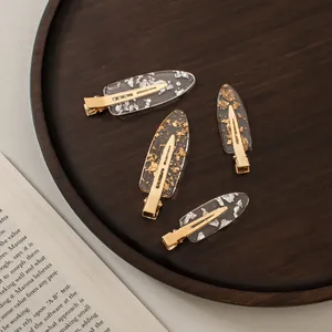 Close-up of four acetate hair clips with gold and silver foil in a wooden tray