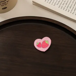 Detail eines rosa Acryl-Herzclips mit Erdbeer-Stickerei auf einem Holztablett