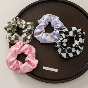 Set of four colorful checkerboard scrunchies displayed on a wooden tray with satin texture