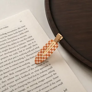Detail of checkered orange and white acetate hair clip placed on a vintage book page