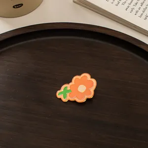 Detailaufnahme einer orangefarbenen Blumenbrosche aus Acryl auf einem Holztablett