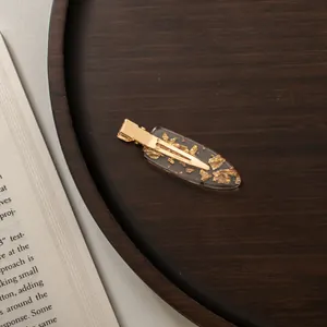 Close-up of a vintage acetate hair clip with gold foil flakes on a wooden tray
