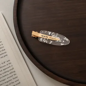 Detailed close-up of a transparent hair clip with silver foil flakes on dark wood