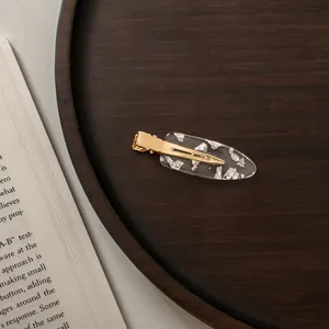 Macro detail of oval acetate hair clip with silver leaf inlay on gold metal base