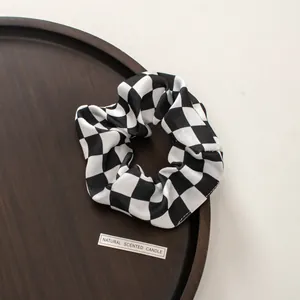 Detail of a black and white checkerboard satin scrunchie on a brown wooden tray