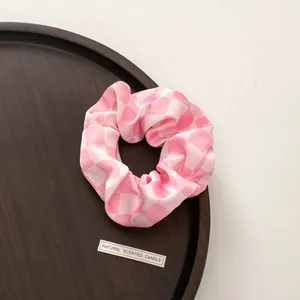 Close-up of pink and white checkered satin scrunchie on a wooden tray accessory