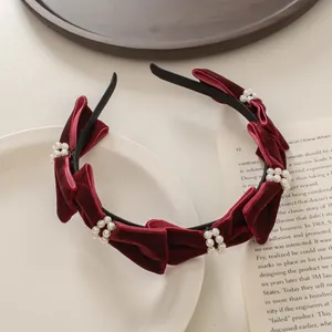 Primer plano de diadema de terciopelo granate con perlas sobre un libro antiguo