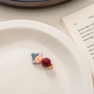 Detail of cute cartoon doll hair clip with blue hat and red pearl on white ceramic tray