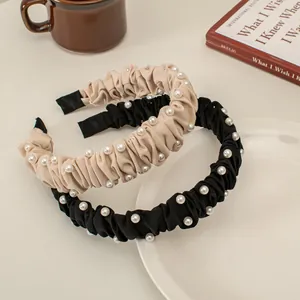 Detailed view of elegant pleated pearl headbands in champagne and black on a ceramic plate