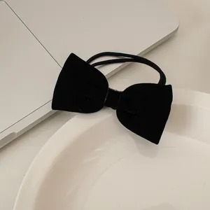 Dettaglio di un elastico per capelli con grande fiocco in velluto nero su un vassoio bianco