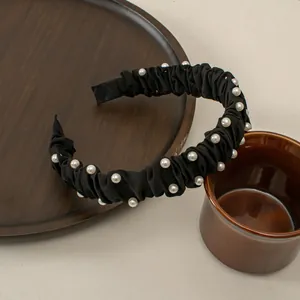 Detail of black pleated headband with white pearls on a rustic wooden tray