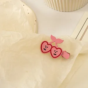 Gros plan d'une pince à cheveux cerise rose en forme de cœur avec un visage souriant doux