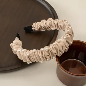 Detailed shot of cream pleated headband with pearls on a rustic wooden tray