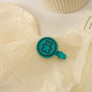 Détail d'une pince à cheveux ours bleu sarcelle mat sur fond texturé beige