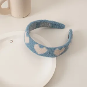 Close-up of blue plush headband with white heart jacquard pattern and soft texture
