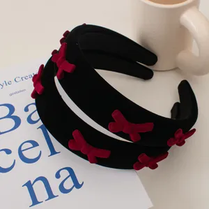 Retro velvet headband with burgundy bows on black padded base beside a white coffee cup