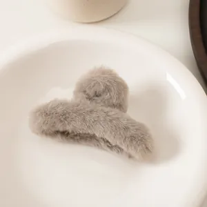 Gros plan d'une pince à cheveux en fausse fourrure taupe sur un plateau en céramique