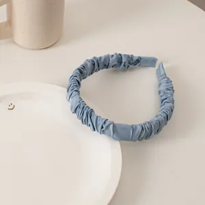 Detail of light blue pleated satin sponge headband on a minimalist white plate
