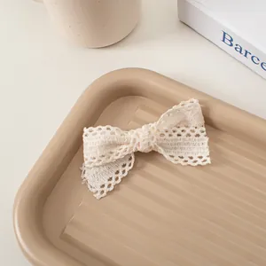 Détail d'une pince à cheveux nœud en dentelle crème avec texture ajourée sur plateau