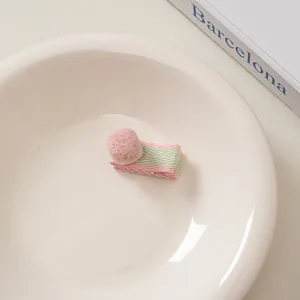 Detail einer süßen Haarspange aus Wollfilz mit rosa Bommeln auf gestrickter Basis