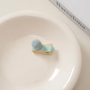 Detail der Haarspange aus Wollfilz mit hellblauem Pompon und gestreiftem Band auf Schale