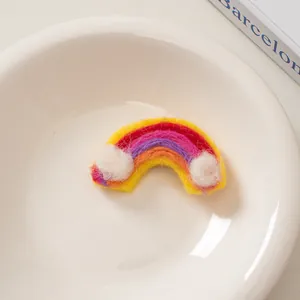 Detail einer bunten Regenbogen-Haarspange aus Wollfilz mit weißen Plüschwolken auf einer Schale
