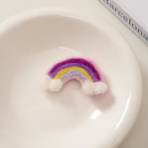 Detailansicht einer bunten Filz-Regenbogen-Haarklammer mit weißen Wolken-Pompons auf Teller