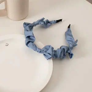 Detail of blue pleated satin headband with a bow on a minimalist white ceramic plate