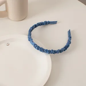 Close-up of pleated Klein blue satin headband on a minimalist white table setup